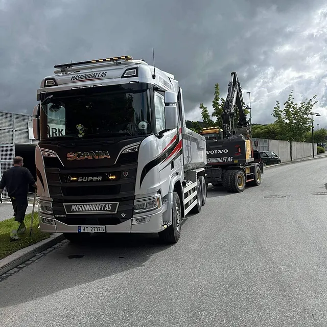 Maskinkraft AS Scania lastebil står parkert med en Volvo gravemaskin lastet bakpå, klart for transport.