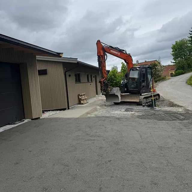 Kompakt gravemaskin står parkert utenfor en enebolig i et boligområde, klar for gravearbeid.